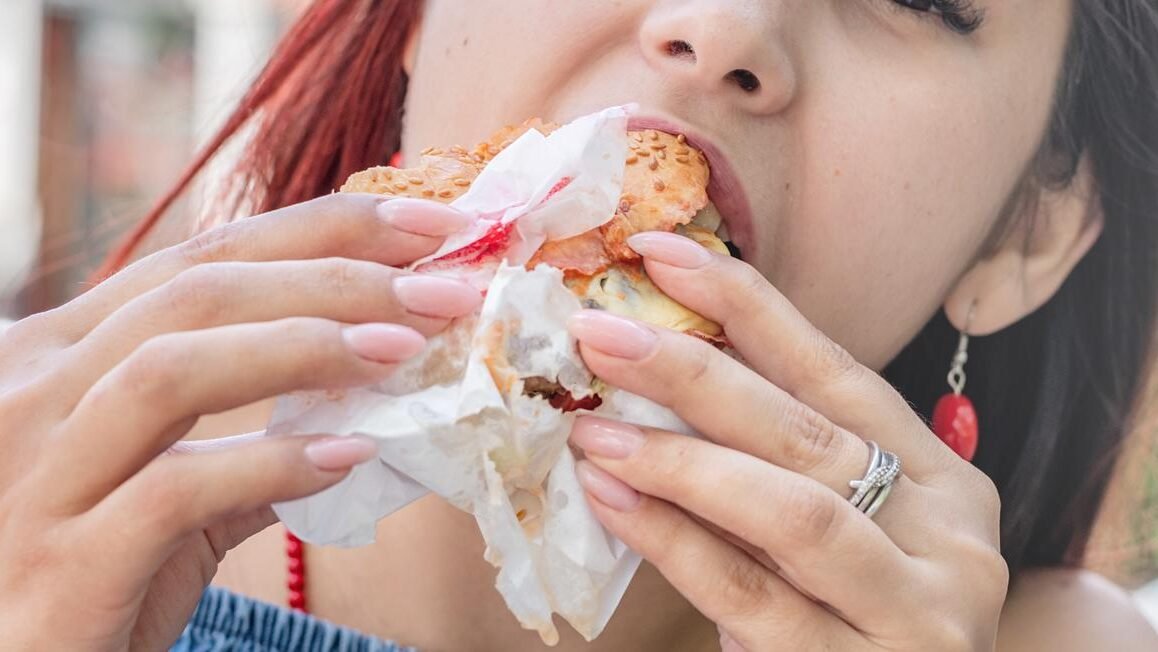 47396670 stylish millennial woman eating burger at street cafe in summer edited