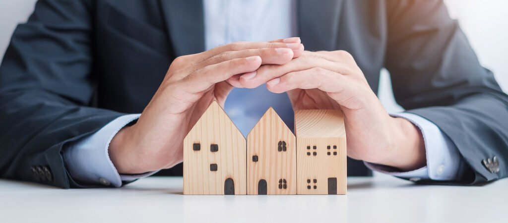 A businessman's hands are holding a wooden model of a house.